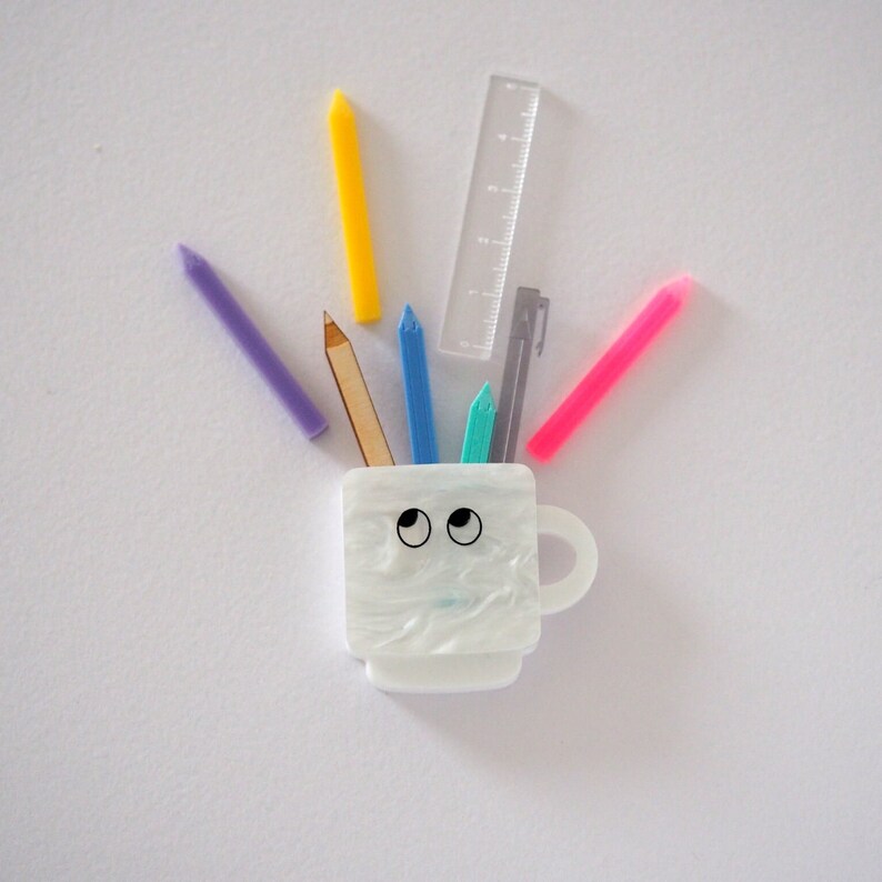 May include: A white ceramic mug with googly eyes and a handle, holding a variety of colorful pencils, crayons, and a ruler.