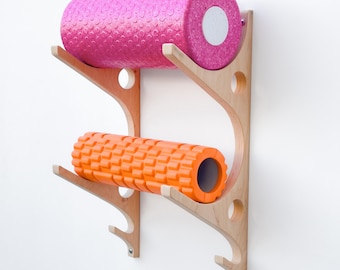 May include: A wooden wall-mounted rack with two foam rollers. The top roller is pink and the bottom roller is orange.