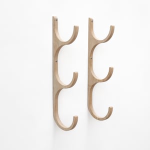 May include: Two wooden wall-mounted coat racks with three hooks each. The racks are made of light-colored wood and have a simple, modern design.