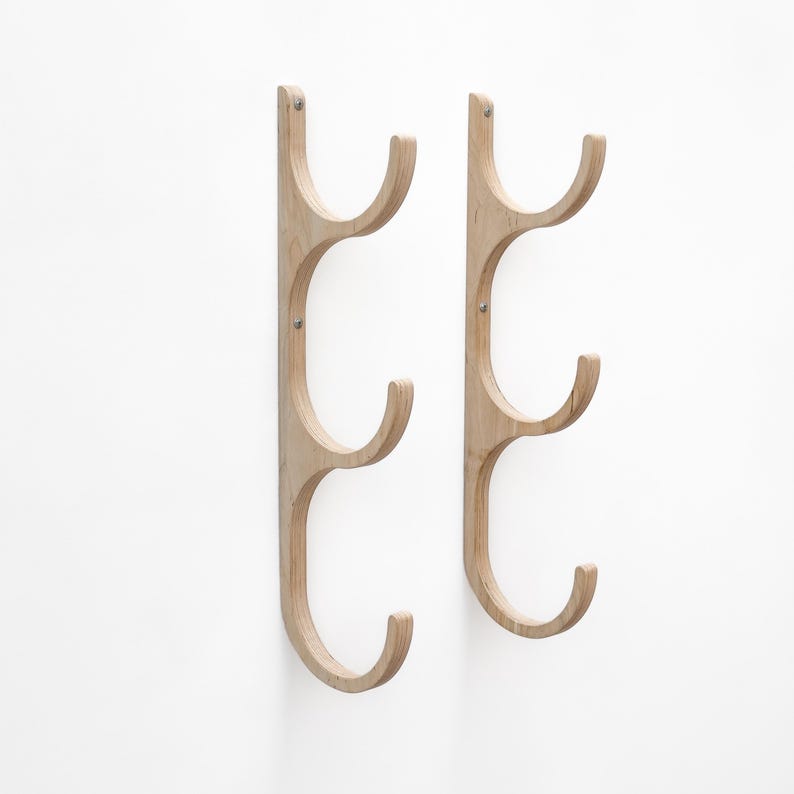 May include: Two wooden wall-mounted coat racks with three hooks each. The racks are made of light-colored wood and have a simple, modern design.