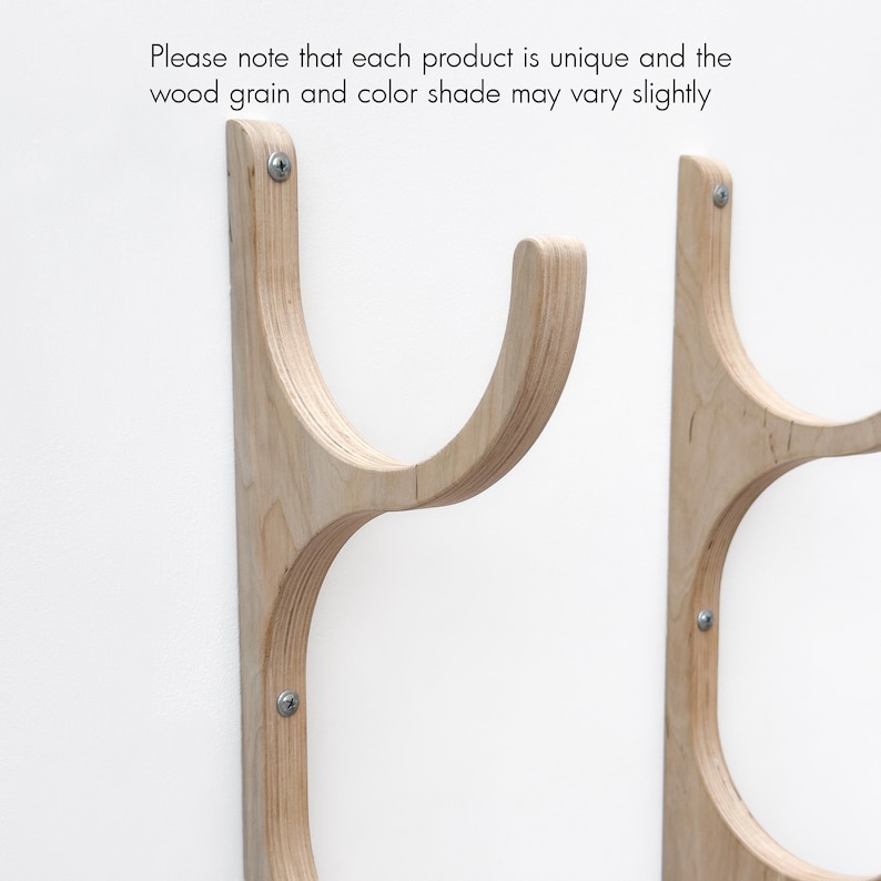 May include: Two wooden wall-mounted surfboard racks with a curved design. The racks are made of light-colored wood and have a natural wood grain.