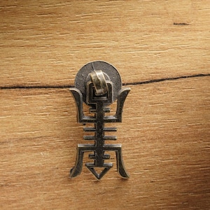 Può includere: Una maniglia per armadio decorativa in metallo con un design intricato. La maniglia è di colore bronzo scuro e ha una parte superiore circolare.