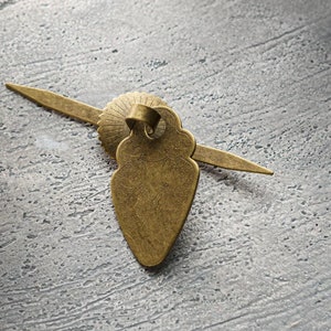 以下が含まれることがあります： 装飾的なデザインが施された金色の金属製のドアノブ。ノブはハート型で、長く、細く、尖った延長部があります。