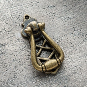 May include: A vintage-style, ornate, gold-toned metal cabinet pull with a decorative, geometric design.
