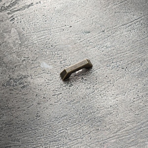 Op de afbeelding: Een kleine, antieke messing kastknop met een rechthoekige vorm en een licht gebogen bovenkant.