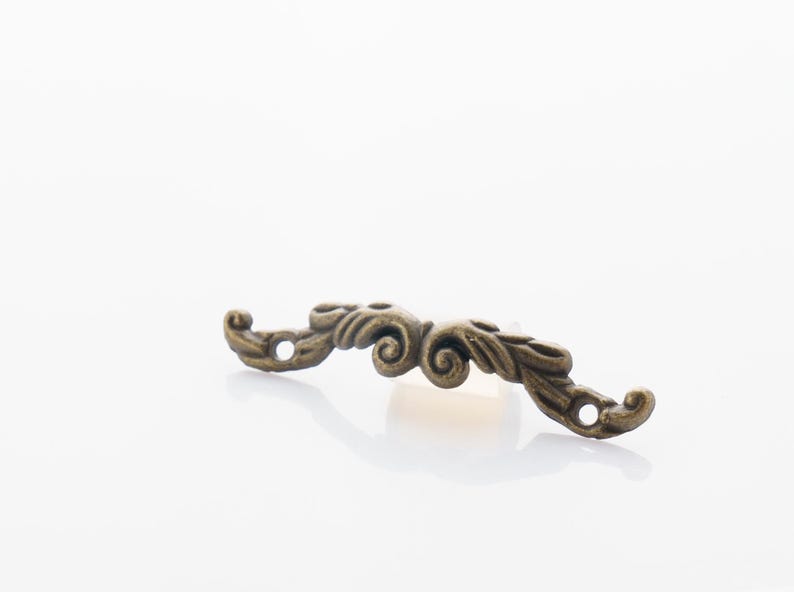 May include: A decorative bronze-colored furniture pull with an ornate, scrolled design. The hardware has two holes for mounting and is curved in shape. Ideal for cabinets, drawers, or other decorative projects.