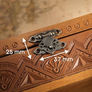 Könnte beinhalten: Nahaufnahme einer Holzkiste mit aufwendigen Schnitzereien und einem Metallverschluss. Die Kiste ist braun, mit einem Verschluss von 37 mm Breite und 25 mm Höhe. Die Kiste hat ein dekoratives Muster.