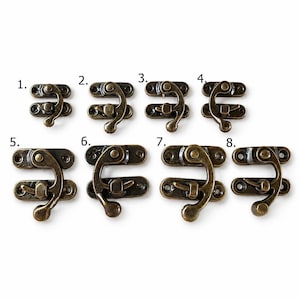 Peut inclure: Huit fermoirs de boîte de couleur bronze antique sont présentés sur un fond blanc. Chaque fermoir est composé d'une base rectangulaire avec des trous de vis et d'un crochet incurvé. Les fermoirs varient en taille et en design, offrant un choix pour divers projets.