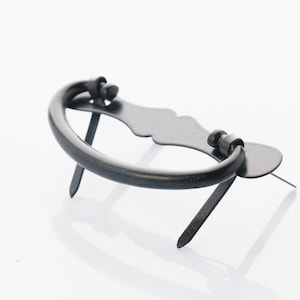 May include: Black metal drawer pull with a curved handle and decorative accents. The pull is mounted on two metal spikes.