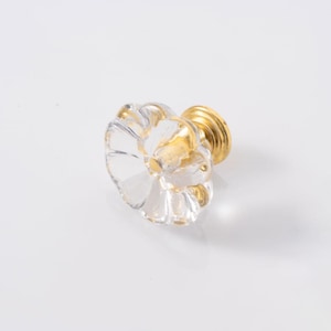 Könnte beinhalten: Schrankknopf aus klarem Glas mit blütenförmigem Design und goldenen Akzenten. Der Knopf hat einen goldenen Sockel und eine transparente, blütenblattförmige Oberseite. Diese dekorative Hardware verleiht jedem Möbelstück Eleganz.