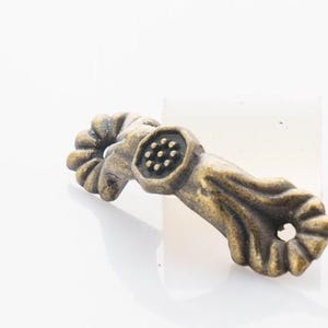 Puede incluir: Tirador de cajón de metal dorado antiguo con un diseño floral decorativo y un centro circular con un patrón texturizado.