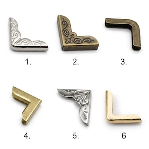 Op de afbeelding: Zes metalen hoekbeschermers voor boeken of dozen, genummerd van 1 tot 6. Item 1 is zilverkleurig met krulwerk, 2 is brons met filigraan, 3 is effen brons, 4 is effen goud, 5 is zilver met bloemreliëf en 6 is een effen gouden hoekstuk.