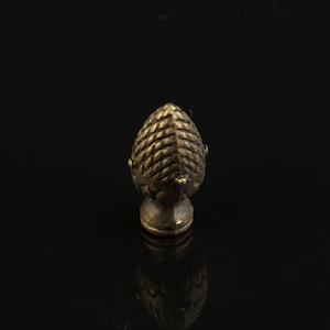 Pode incluir: Um pequeno acabamento de metal dourado com um design texturizado detalhado que se assemelha a uma pinha.