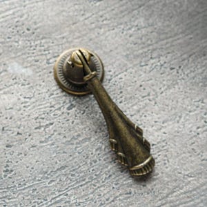 May include: An ornate, bronze-coloured cabinet pull with a decorative, pointed handle, in a vintage style.