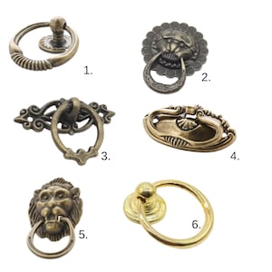 May include: A selection of six antique bronze cabinet pulls. The designs include a ring pull with a textured handle, a lion's head with a ring pull, and ornate oval and round pulls. These decorative pulls are suitable for furniture restoration projects.