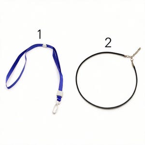 Puede incluir: Un cordón azul para el cuello marcado con el número 1, con un conector de plástico blanco y un gancho giratorio blanco. Junto a él, un collar de cordón negro marcado con el número 2, con un cierre de mosquetón y cadena de metal plateado.
