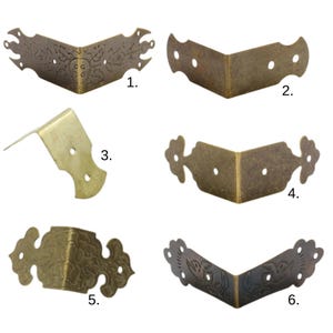 May include: A collection of six antique brass-toned corner brackets. Each bracket is L-shaped, with varying decorative designs, including floral patterns and bird motifs. Some have rounded edges, while others are more angular.