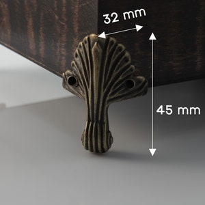 Op de afbeelding: Close-up van een decoratieve metalen meubelpoot met een waaiervormig ontwerp. De poot is 32 mm breed en 45 mm hoog.