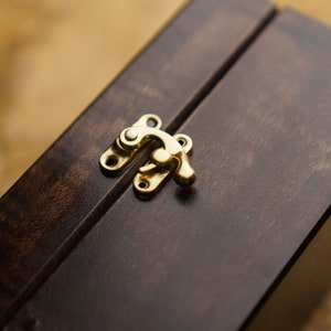 May include: A dark brown wooden box with a gold metal latch. The box is closed.