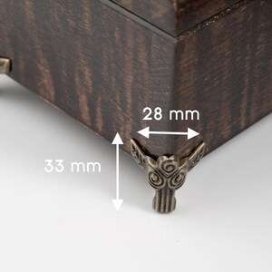 May include: Close-up of a dark brown wooden box corner with decorative bronze-coloured corner feet. The box is 2.8 cm wide and the feet are 3.3 cm tall. The wood grain is visible.