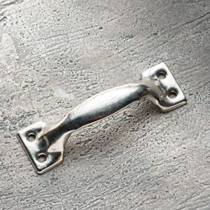 May include: A silver metal door handle with a curved design. The handle is on a grey textured surface.
