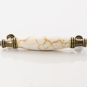 Op de afbeelding: Een witte keramische kastknop met een bruin marmerpatroon en antieke messing accenten.