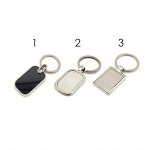 Op de afbeelding: Drie metalen sleutelhangers gelabeld 1, 2 en 3. Sleutelhanger 1 heeft een zwart rechthoekig label met afgeronde hoeken. Sleutelhanger 2 heeft een zilverkleurig rechthoekig label. Sleutelhanger 3 heeft een geborsteld zilveren rechthoekig label.