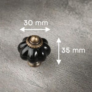 May include: Black and brass cabinet knob with a flower-like design. The knob is 3.5 cm tall and 3 cm wide. The hardware has a glossy finish and is suitable for drawers and cabinets.