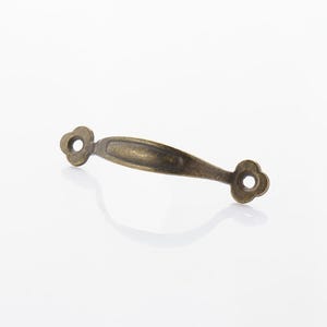 May include: Antique brass-toned drawer pull with a curved handle and decorative floral-shaped ends. The hardware is designed for cabinets, drawers, or furniture. The pull measures approximately 4 inches in length.