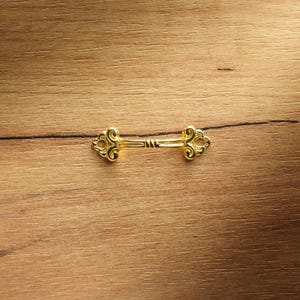 Pode incluir: Uma puxador de gaveta de metal dourado com um design decorativo de buraco de fechadura.