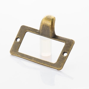 May include: Antique brass drawer pull with a rectangular label holder. The pull has a decorative, curved top.
