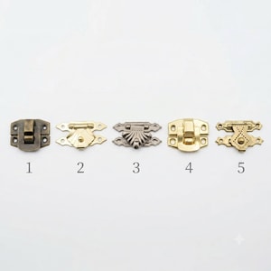May include: Five metal box latches arranged in a row, labeled 1 through 5. The latches vary in finish, including antique bronze, brass, and silver tones, and feature distinct decorative shapes, including shell-like designs and rectangular plates.