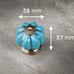 May include: A turquoise ceramic cabinet knob with a bronze base and center. The knob is 3.7 cm tall and 3.8 cm wide. The knob has a flower-like design with bronze accents.