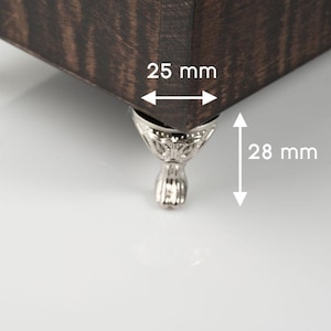 May include: Close-up of a dark brown wooden box corner with decorative silver-colored feet. The box corner measures 25 mm wide and the feet are 28 mm tall. The wood grain is visible.
