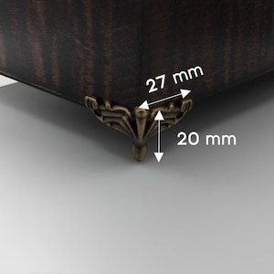 May include: Close-up of a dark brown wooden box corner with a decorative bronze-colored metal foot. The foot is 20 mm high and 27 mm wide. The wood grain is visible.