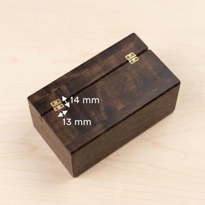 May include: A dark stained wooden box with a hinged lid and brass-colored hardware. The box measures 13 mm x 14 mm. The box is rectangular and has a smooth, polished finish. The box is closed.