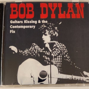 Op de afbeelding: Een CD-hoesje van Bob Dylan met de albumtitel "Guitars Kissing & the Contemporary Fix" in rode letters. De hoes toont een zwart-wit afbeelding van Bob Dylan die gitaar speelt en zingt.