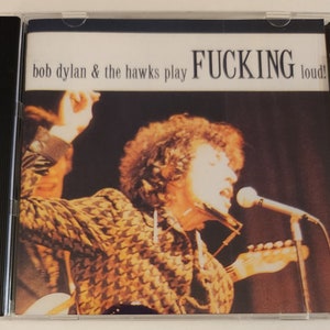 May include: A CD cover featuring a black and white photo of Bob Dylan playing a harmonica and singing into a microphone. The text on the cover reads "bob dylan & the hawks play FUCKING loud!"