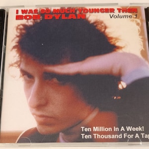 Puede incluir: Una funda de CD de Bob Dylan con el título del álbum "I Was So Much Younger Then" y "Volume 1" en rojo. La portada presenta una imagen en tonos sepia de Bob Dylan. También se ve el texto "Ten Million In A Week! Ten Thousand For A Tape!"