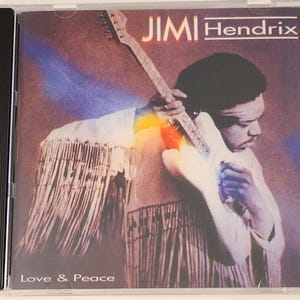 May include: A CD case featuring a colorful image of Jimi Hendrix playing a white electric guitar. The text "Jimi Hendrix" is printed in white on a black background. The text "Love & Peace" is printed in white at the bottom of the case.