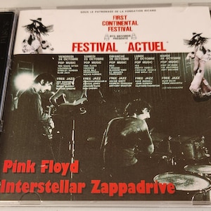 Può includere: Una copertina di CD con una foto in bianco e nero di una band che suona sul palco. Il testo sulla copertina recita "Pink Floyd Interstellar Zappadrive" e "First Continental Festival".