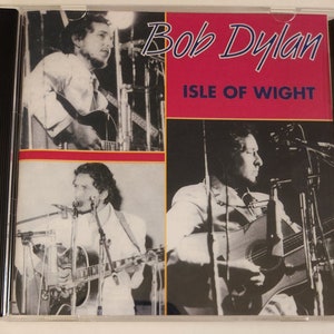 May include: A CD case with a black spine and a clear front cover. The front cover features a black and white photo of Bob Dylan playing a guitar. The text "Bob Dylan" and "Isle of Wight" is printed in blue and white on a red background.