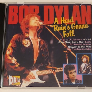Puede incluir: Una caja de CD con una imagen roja y blanca de Bob Dylan tocando la guitarra. El título del álbum es "A Hard Rain's Gonna Fall" y la portada del álbum presenta una lista de canciones que incluyen "Visions of Johanna", "It's All Over Now", "Baby Blue Boots", "Of Spanish Leather", "Blowin' In The Wind" y "Mr. Tambourine Man".