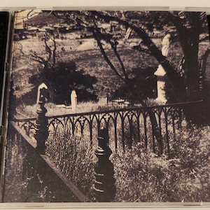 May include: A black and white photo of a cemetery with a wrought iron fence and a tree in the background.