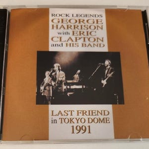 May include: A CD case with a photo of George Harrison, Eric Clapton, and their band on stage. The text on the case reads "Rock Legends George Harrison with Eric Clapton and His Band Last Friend in Tokyo Dome 1991".