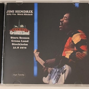 Può includere: Una copertina di CD con Jimi Hendrix che suona la chitarra. La copertina è blu e bianca con il testo "Jimi Hendrix, Billy Cox, Mitch Mitchell, Gröna Lund, Stora Scenen, Grona Lund, Stockholm, 31.8 1970, High Fidelity" stampato su di essa.