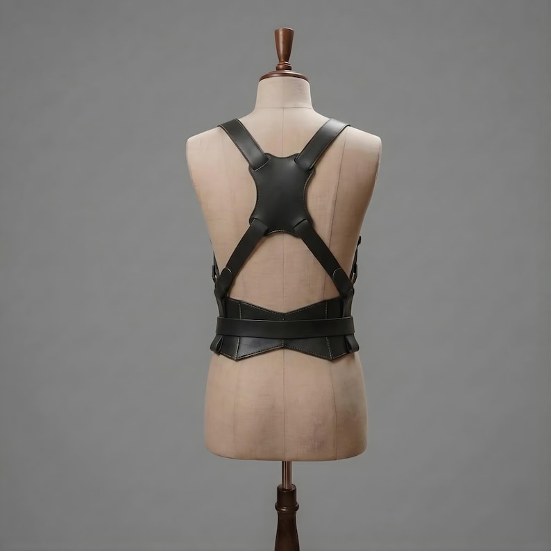 May include: A black leather harness featuring a central back panel with four straps extending over the shoulders and around the waist. The structure includes a horizontal waist belt connected to the back piece, creating a geometric, symmetrical design.