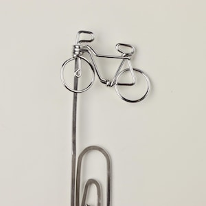 May include: Silver wire bookmark shaped like a bicycle with a paperclip attached to the bottom.