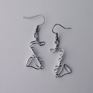 Peut inclure: Une paire de boucles d'oreilles en argent en forme de saxophone. Les boucles d'oreilles sont en fil de fer et ont un design simple et moderne.