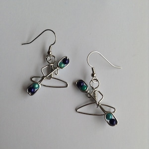 May include: A pair of silver wire earrings shaped like a person in a canoe with blue and teal beads.